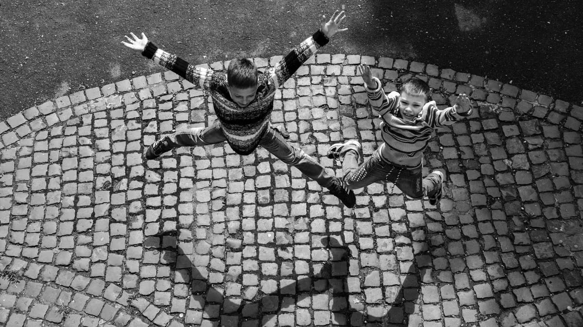 Two children jumping on a cobblestone surface in Lviv, Ukraine, captured in black and white from above.